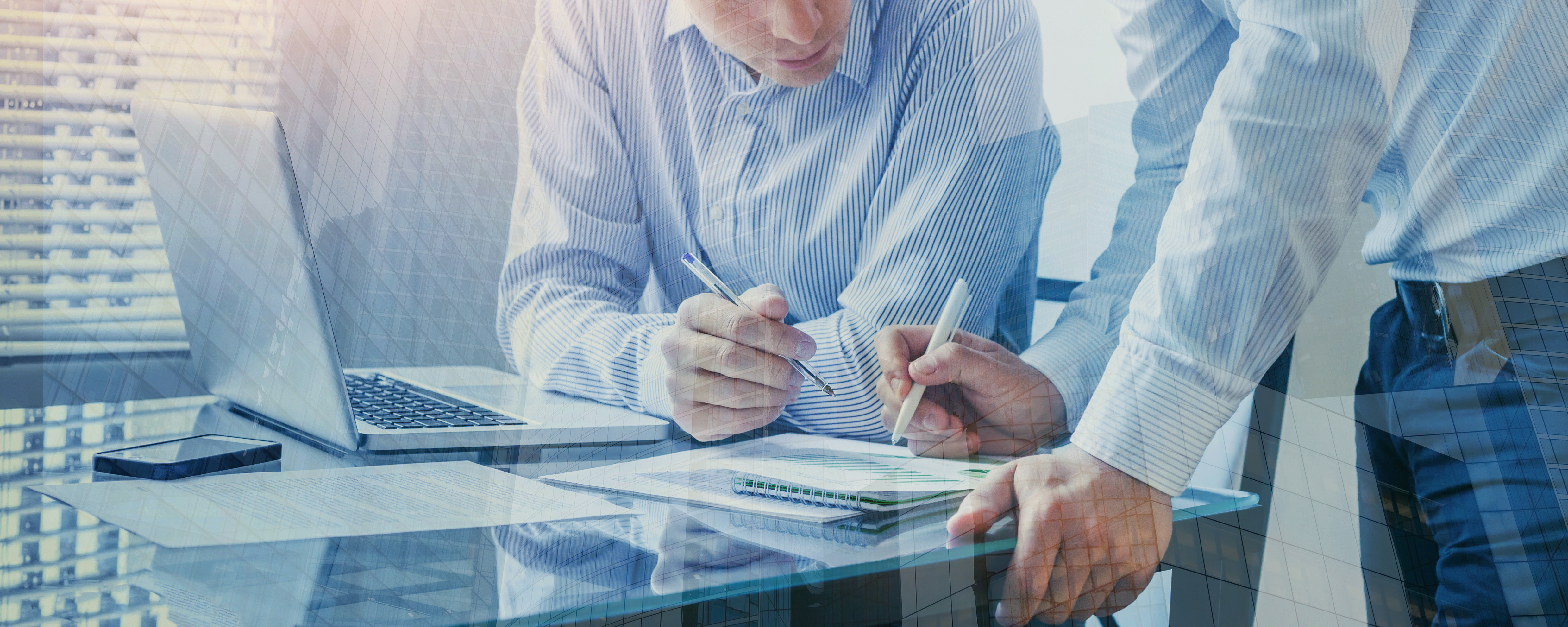 two people standing over desk looking at paperwork and computer